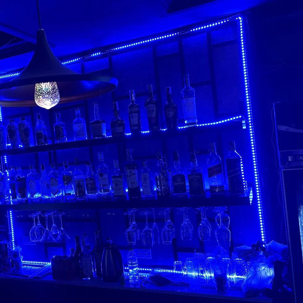 Back bar shelves of spirits and glasses lit in blue LED